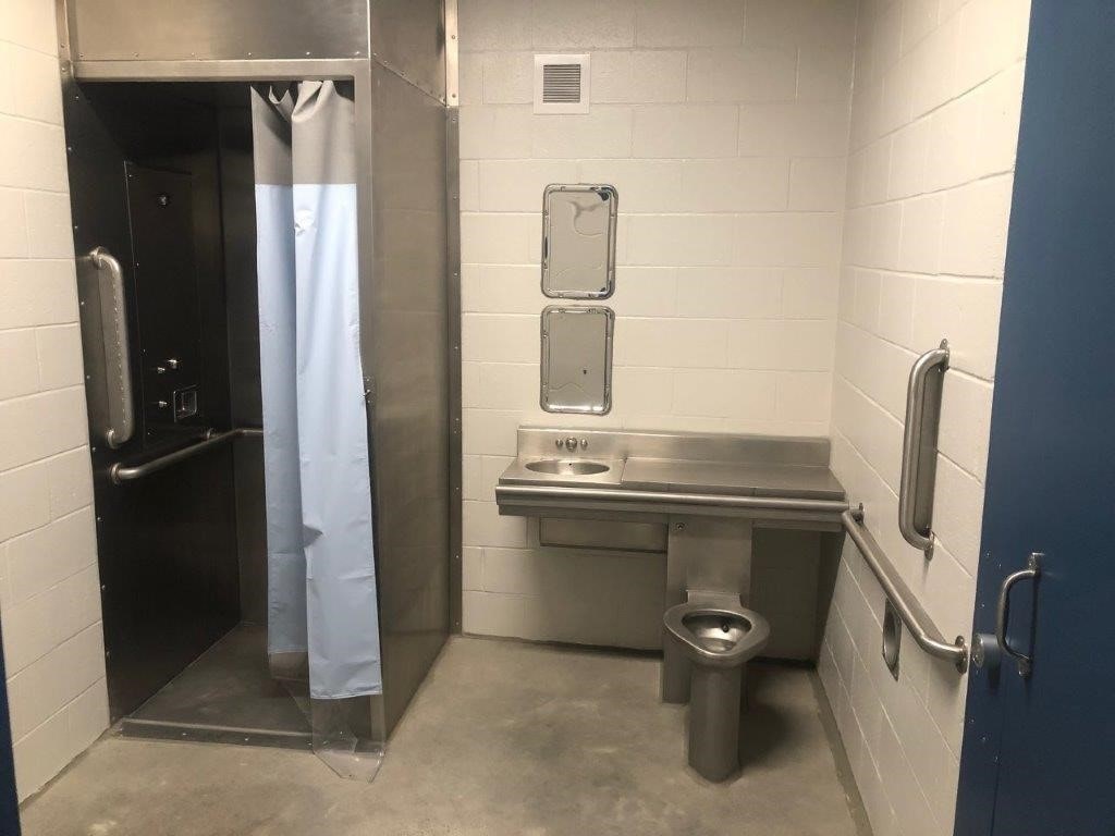 This image depicts Willoughby Industries products including a shower, mirror, combination sink and toilet installed within a prison cell.